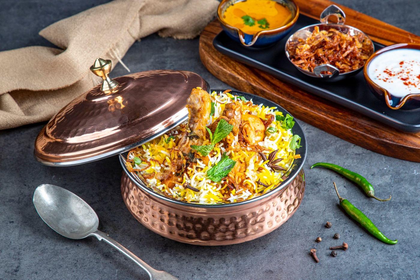 Chicken biryani served in a copper handi with raita and curry sauce